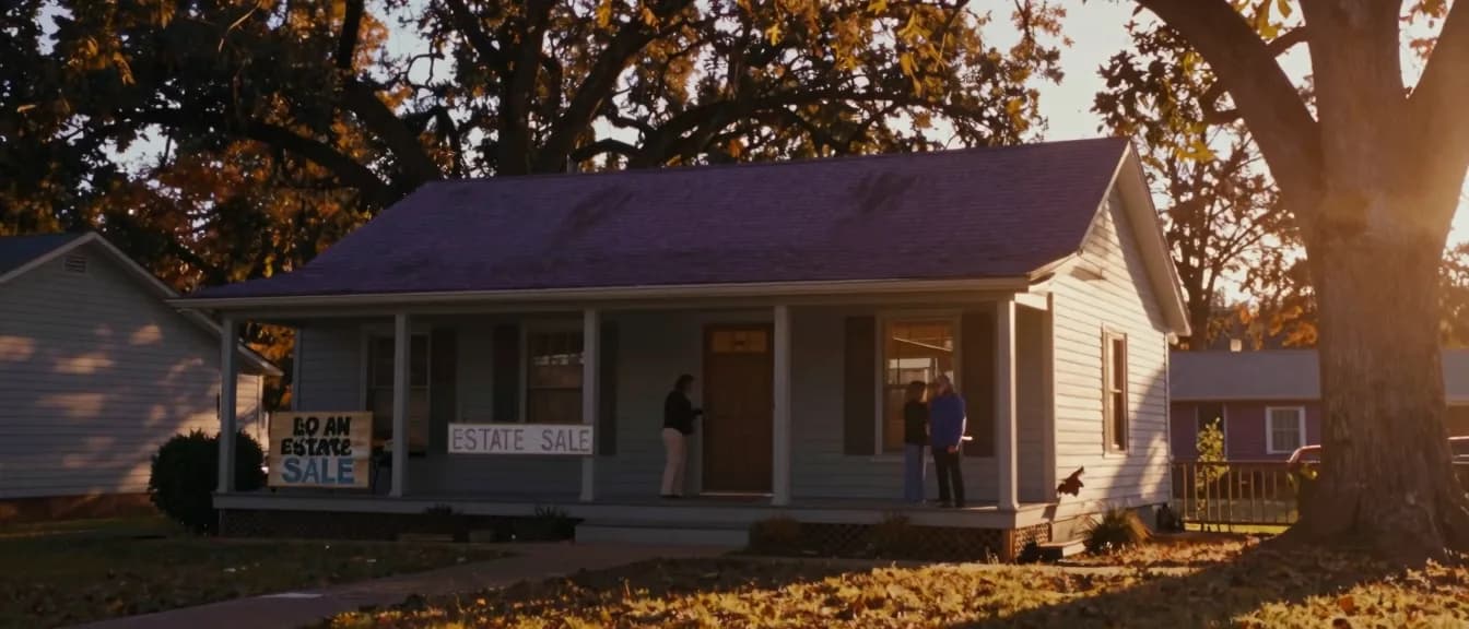 A single-story home held open for an estate sale under mature oaks