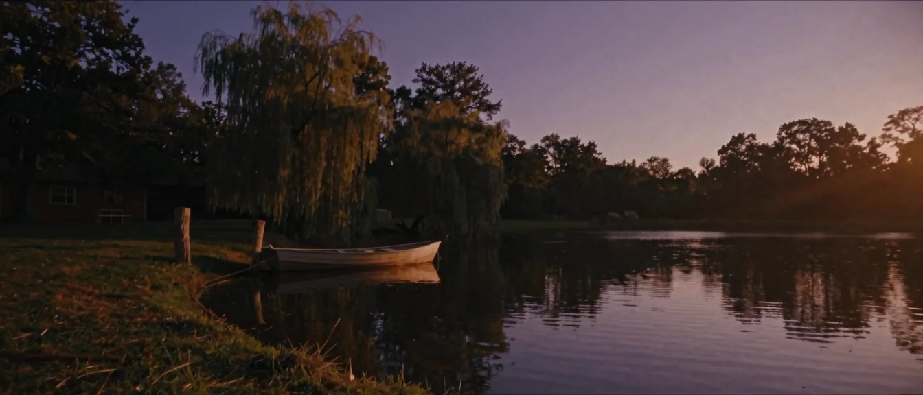 A wooden rowboat tied at the bank of a rural farm pond at dusk