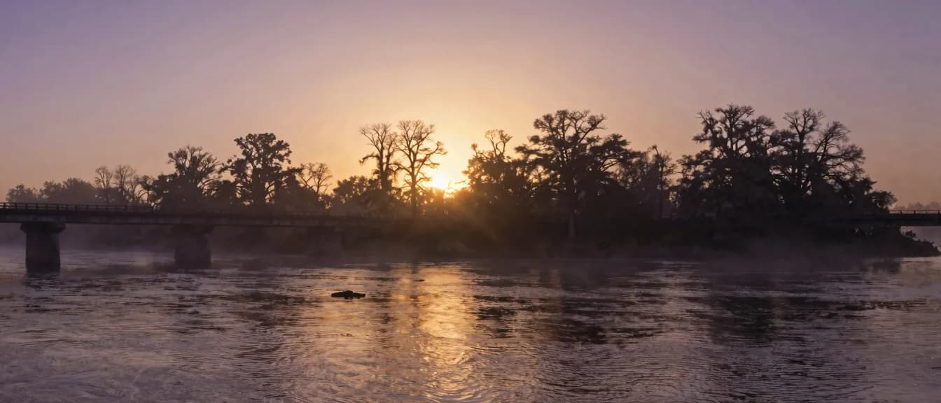 A two-lane bridge crossing a wide river at dawn