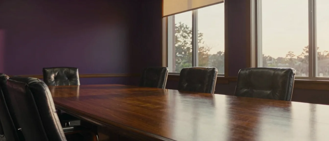 An empty boardroom table running the length of a windowed room